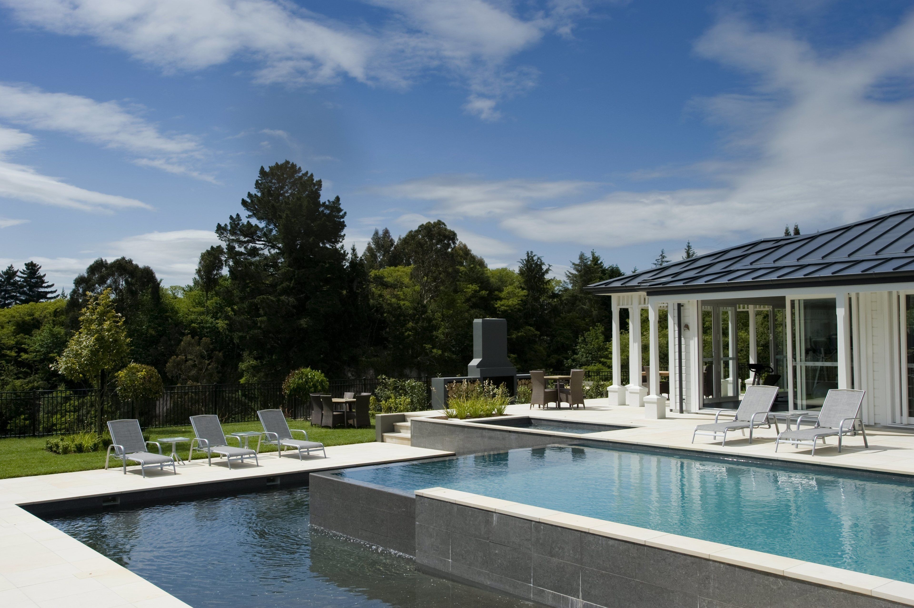 A modern outdoor pool area with lounge chairs, a barbecue area, and a glass-enclosed patio.