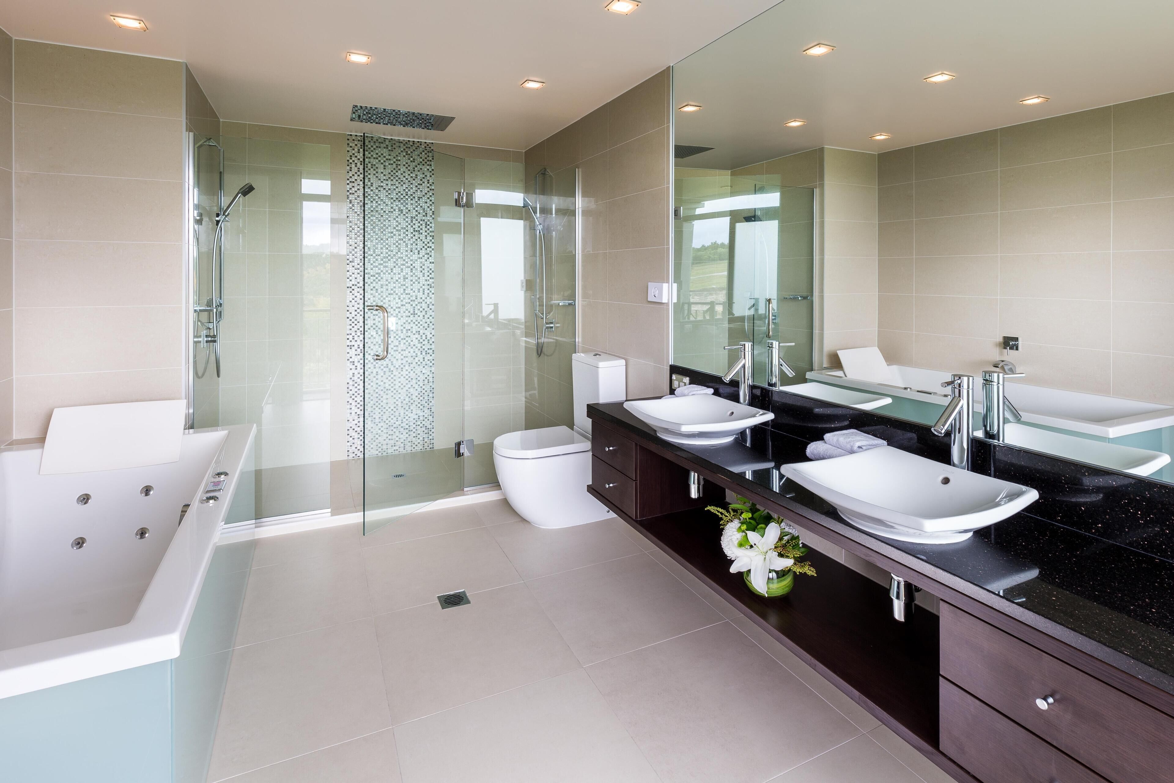 Une salle de bain moderne dotée d’une douche à parois de verre, d’une baignoire blanche et d’un meuble-lavabo double avec un grand miroir.