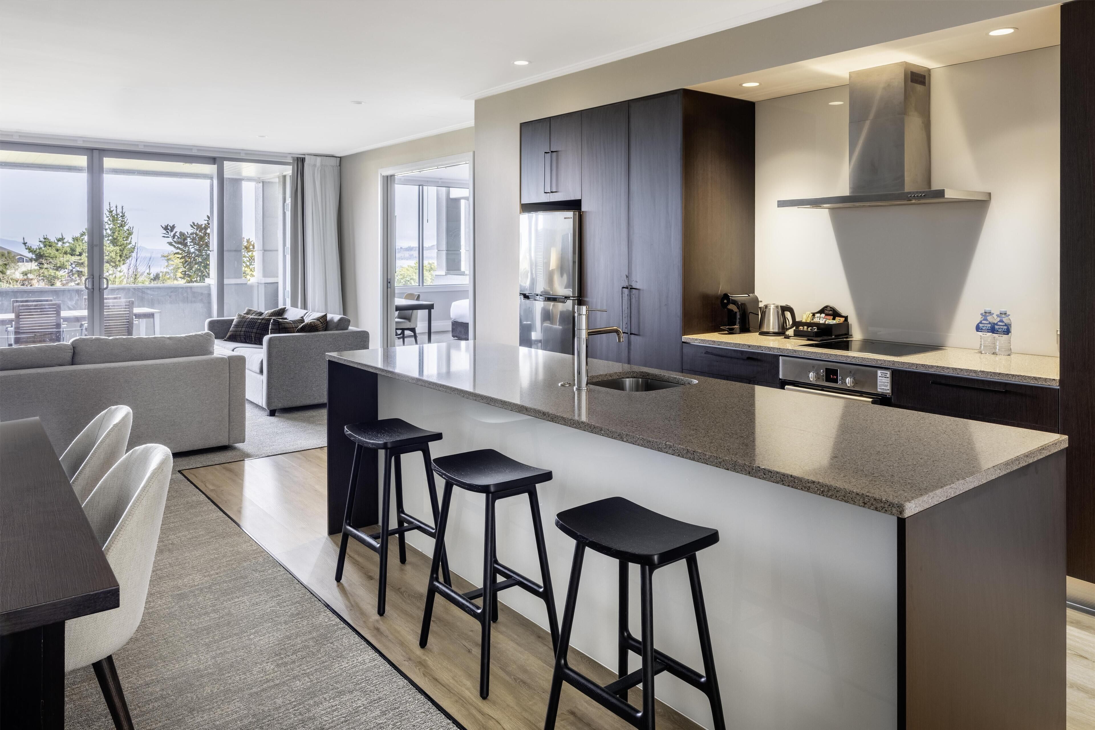 A modern kitchen with a large island, bar stools, and a built-in oven.