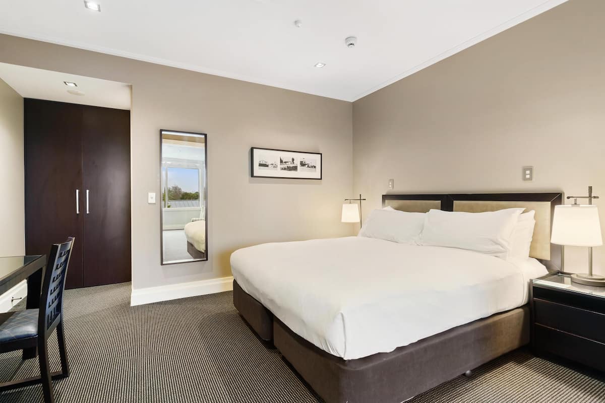 Une chambre d’hôtel avec un grand lit, un bureau, une chaise, une armoire et un tableau encadré au mur.