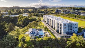 A modern multi-story hotel with a swimming pool, surrounded by lush greenery and hilly terrain.