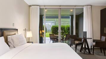 Une chambre d’hôtel avec un grand lit, un bureau avec deux chaises, un ordinateur portable et une vue sur un jardin, accessible par une porte-fenêtre coulissante.