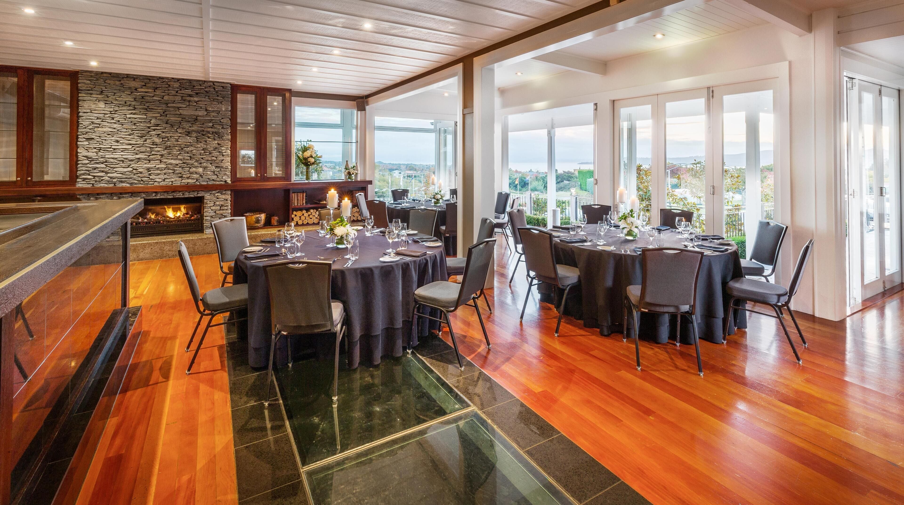 Un restaurant avec des tables rondes disposées pour le service, un mur en pierre et une cheminée.