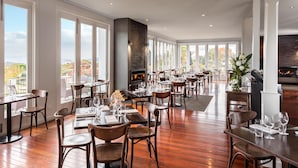 A spacious restaurant with high ceilings, large windows, and a fireplace. Tables are set with wine glasses and plates.