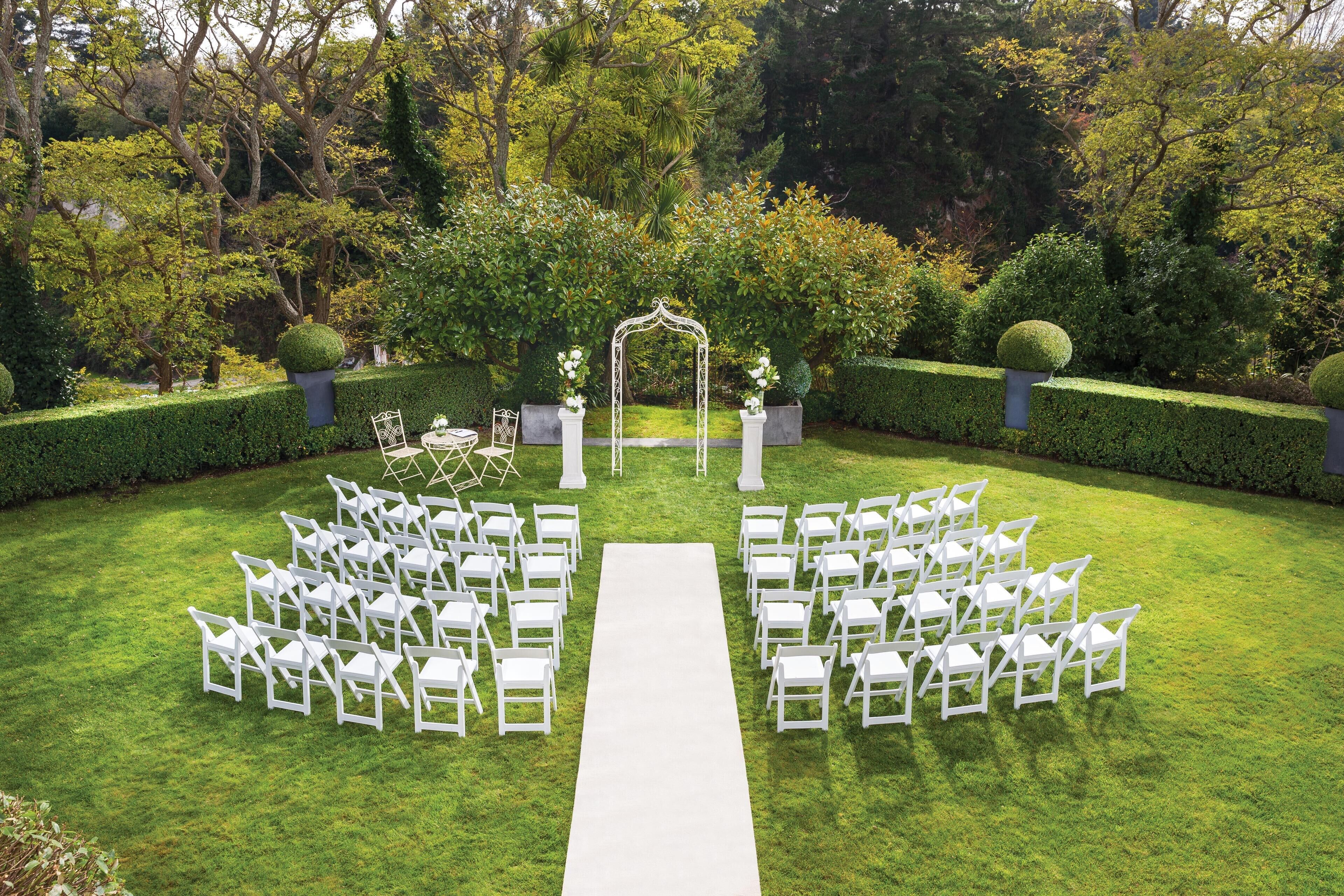 Un espacio al aire libre con jardín, con un pasillo blanco y sillas dispuestas para un evento.