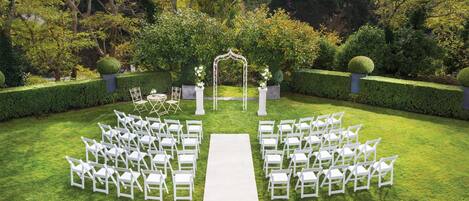 A garden venue with a white aisle and chairs arranged for an event.