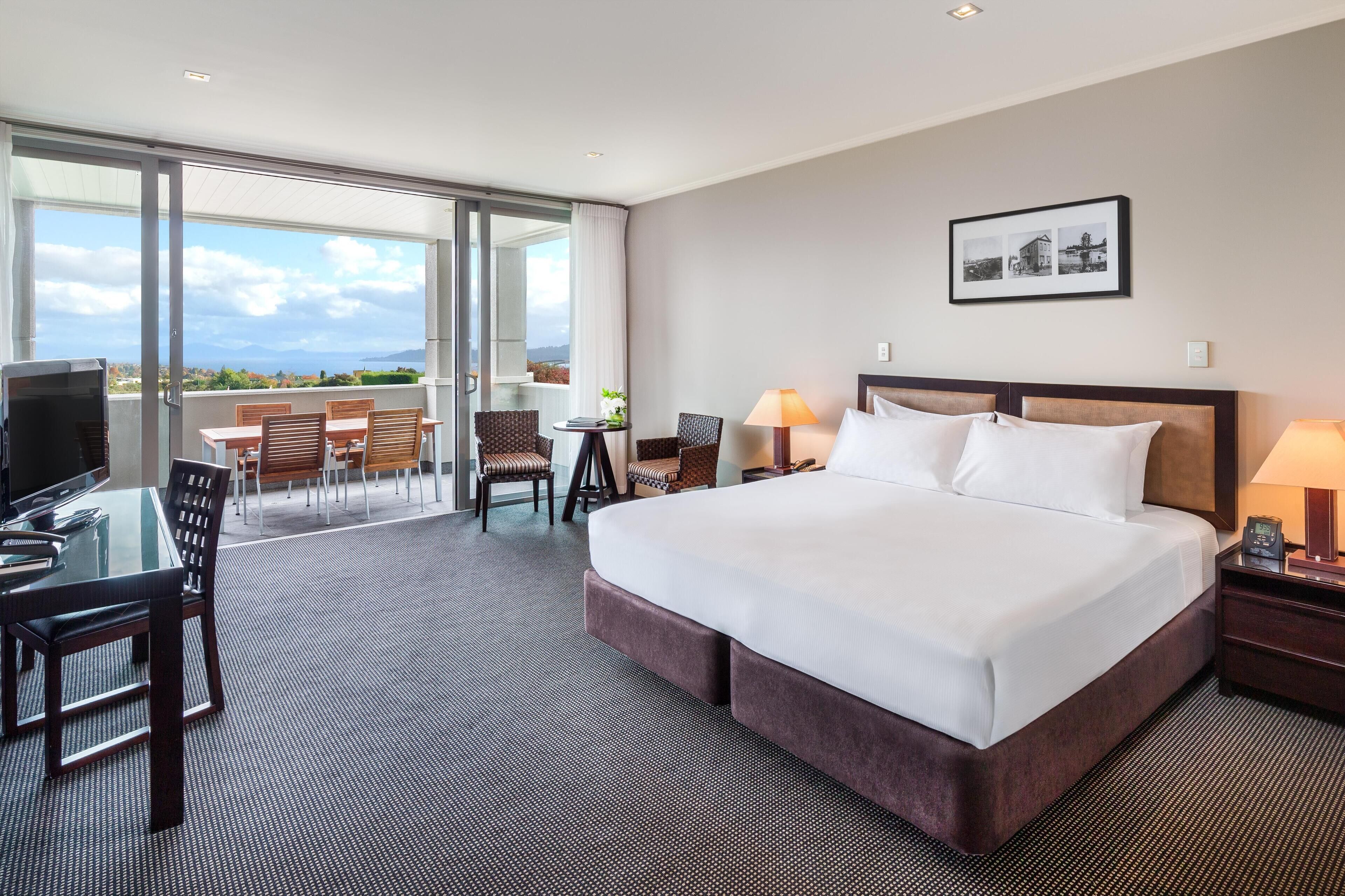 A hotel room with a large bed, a desk, a TV, and a balcony with a view.