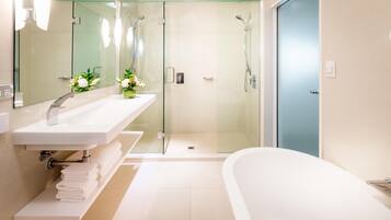 Un baño moderno con ducha de vidrio, bañera blanca y tocador con espejo y lavamanos.