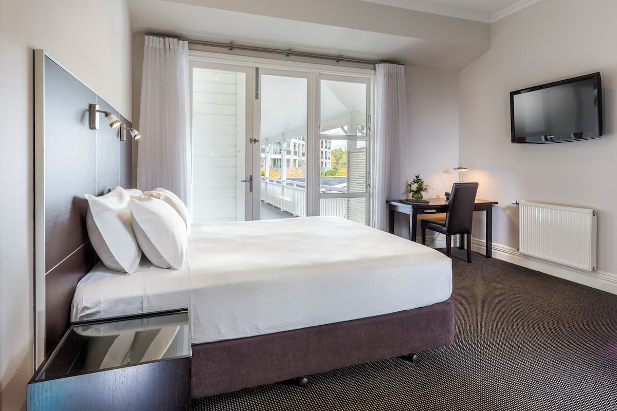 A hotel room with a bed, a desk, a chair, a TV, and a view of the outside.