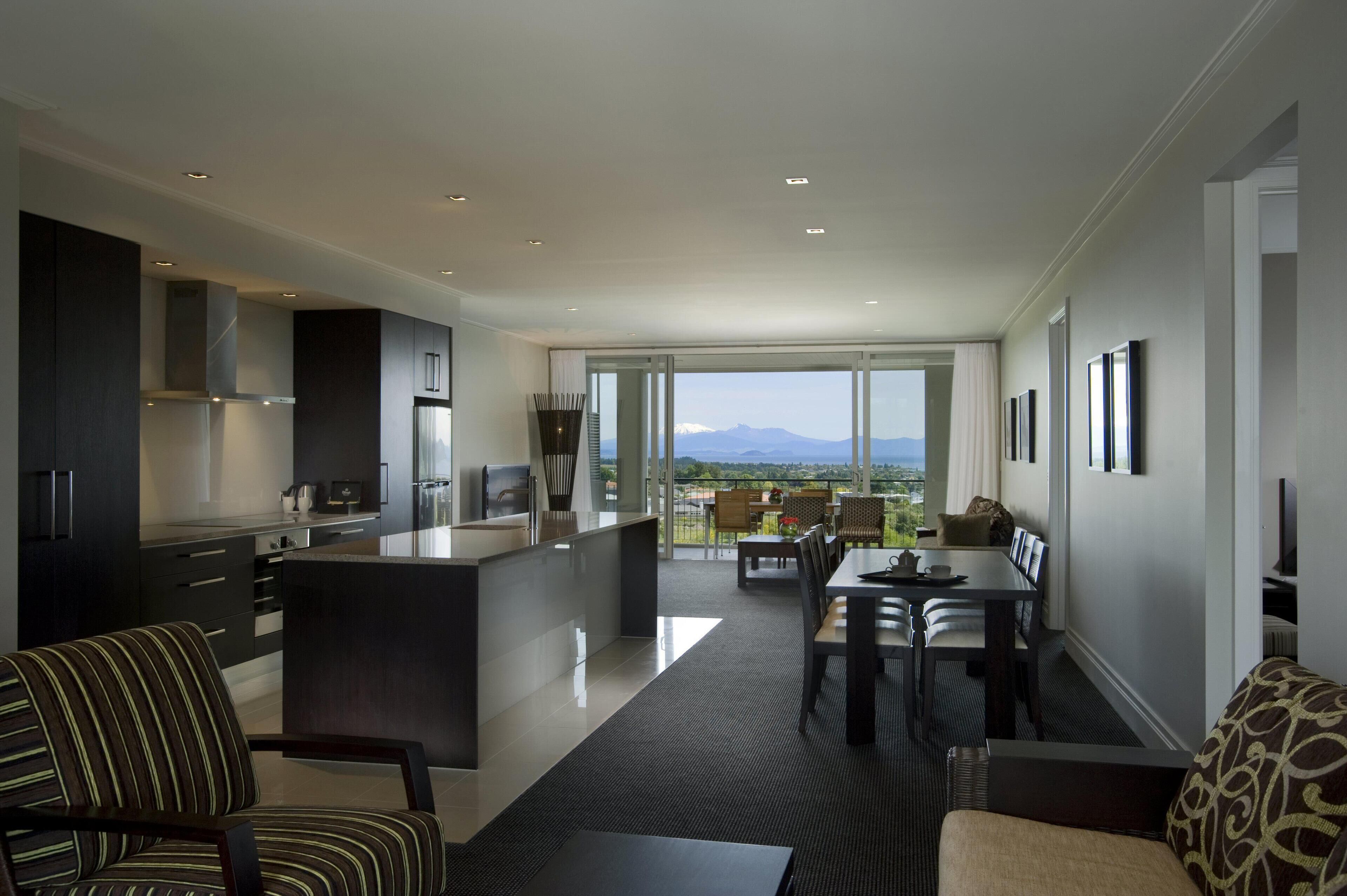 Una cocina moderna con una isla central, comedor con vistas y un balcón con la silueta de montañas.