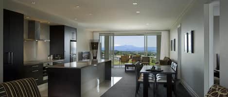Una cocina moderna con una isla central, comedor con vistas y un balcón con la silueta de montañas.
