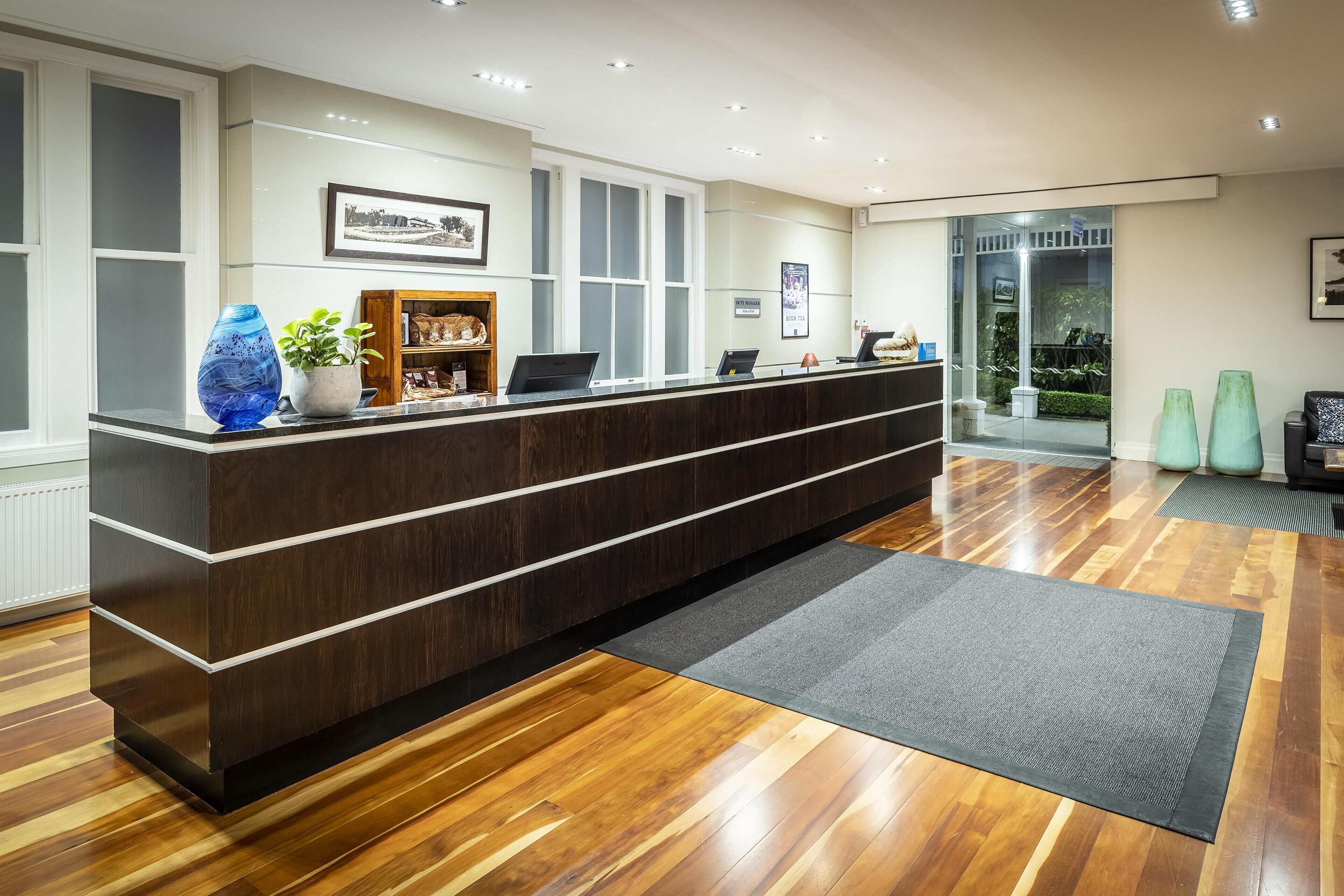 A reception desk with a dark wood finish, a potted plant, and a framed picture on the wall.