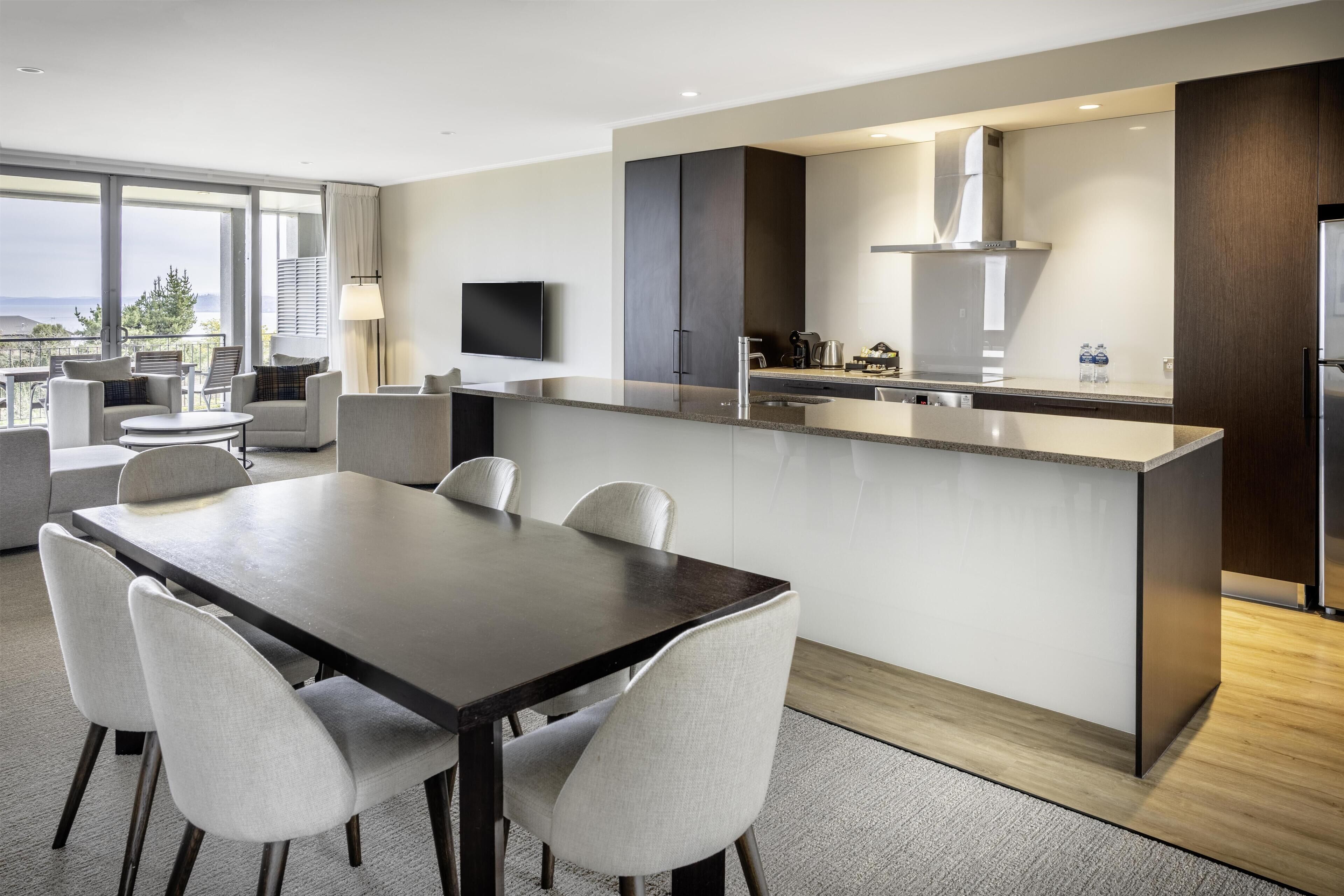 Una cocina moderna con una isla central, un comedor con mesa y sillas, y una sala de estar con sofá y sillones.