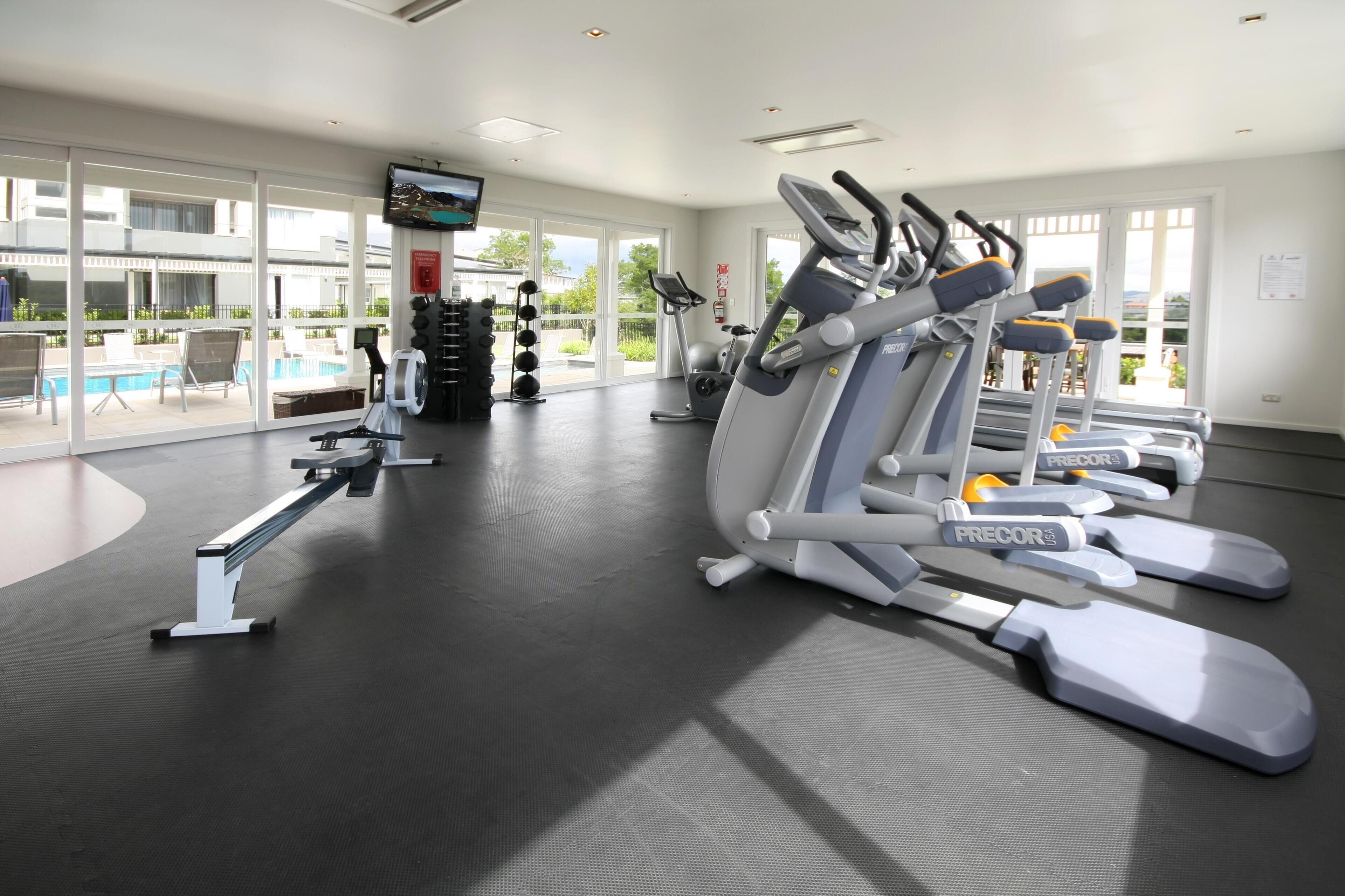 A gym with treadmills, weight machines, and a pool area visible through large windows.