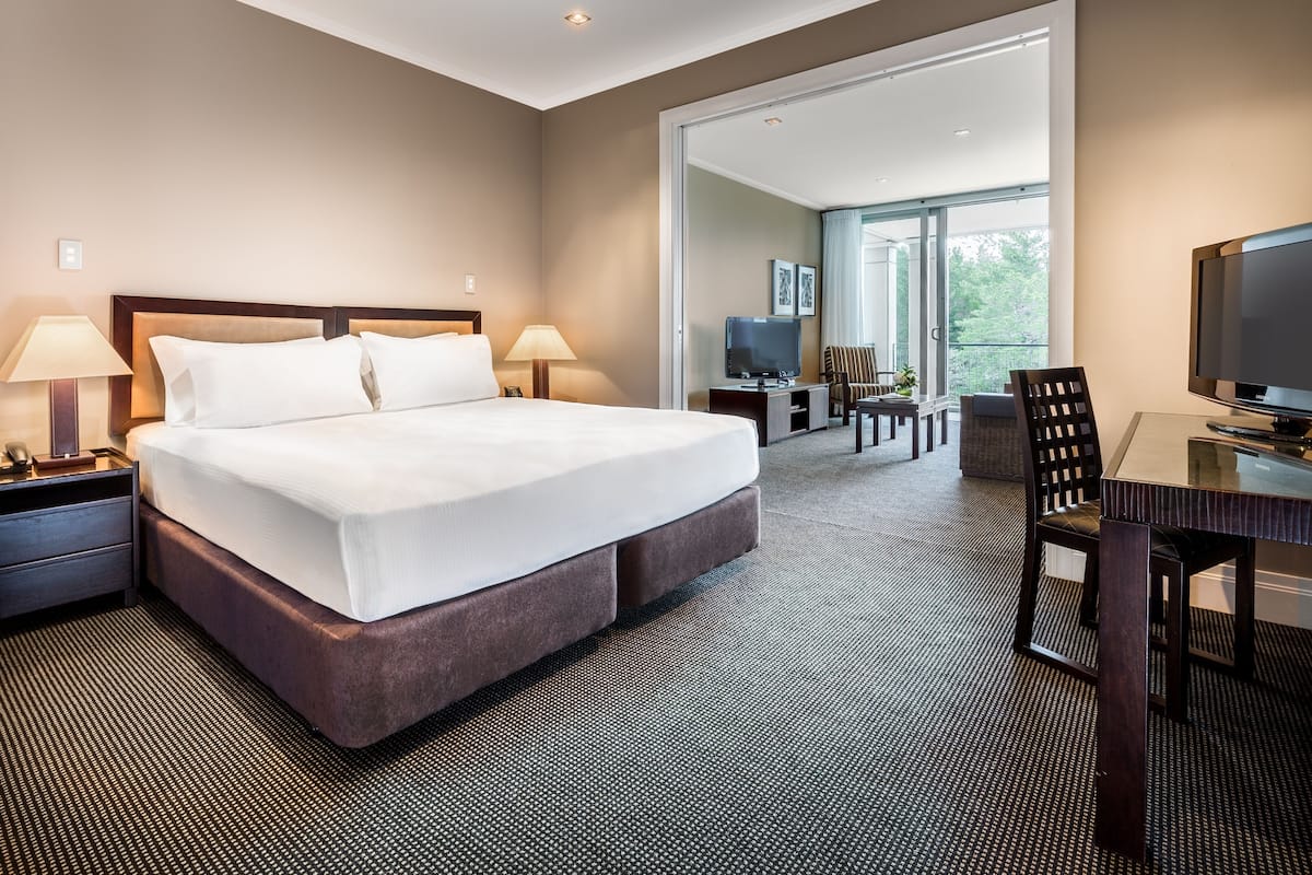 A hotel room with a large bed, bedside lamps, a desk with a chair, a television, and a view of the outdoors.