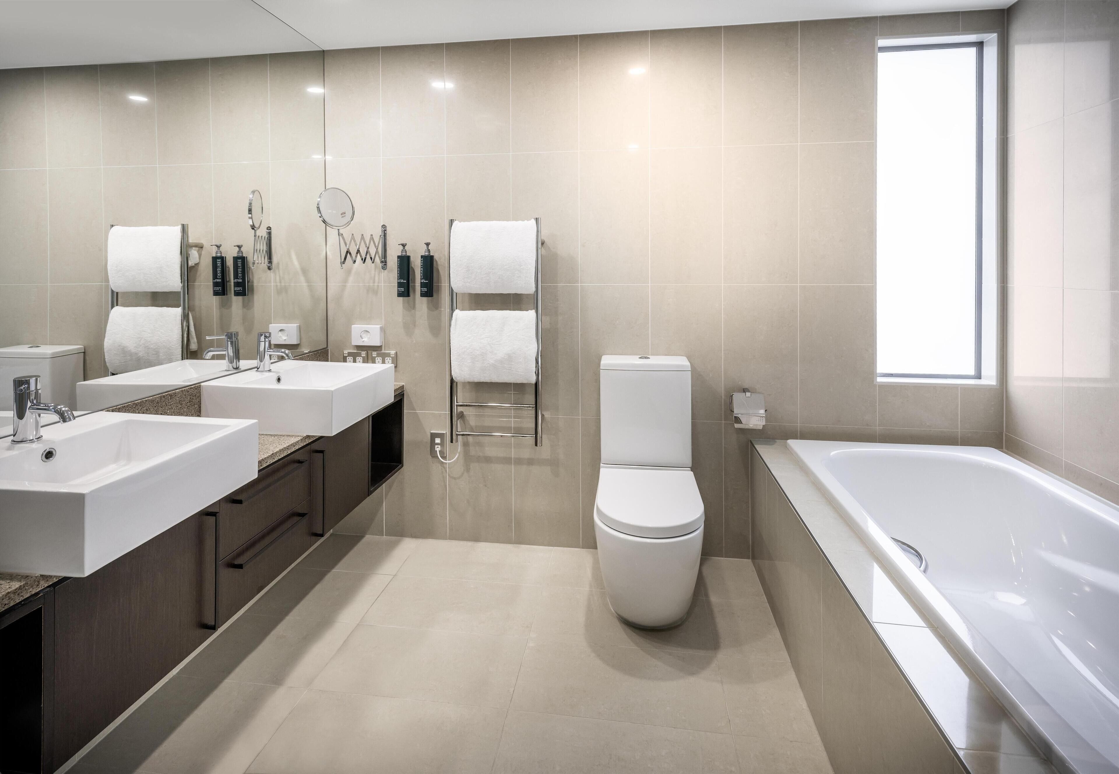 Un baño moderno con un lavabo grande, dos espejos, un inodoro y una bañera.
