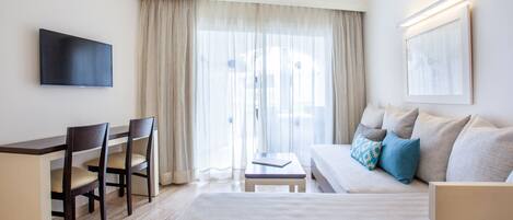 A hotel room with a bed, a desk with chairs, a television, and a large window with curtains.
