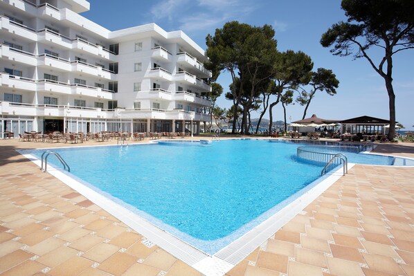 A swimming pool with tiled deck, surrounded by outdoor seating and a multi-story building. - Grupotel Los Príncipes & Spa (Muro)
