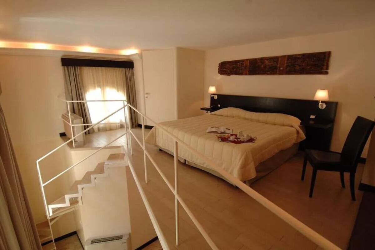Una habitación de hotel con una cama, una silla, una mesita de noche, una lámpara y una escalera.