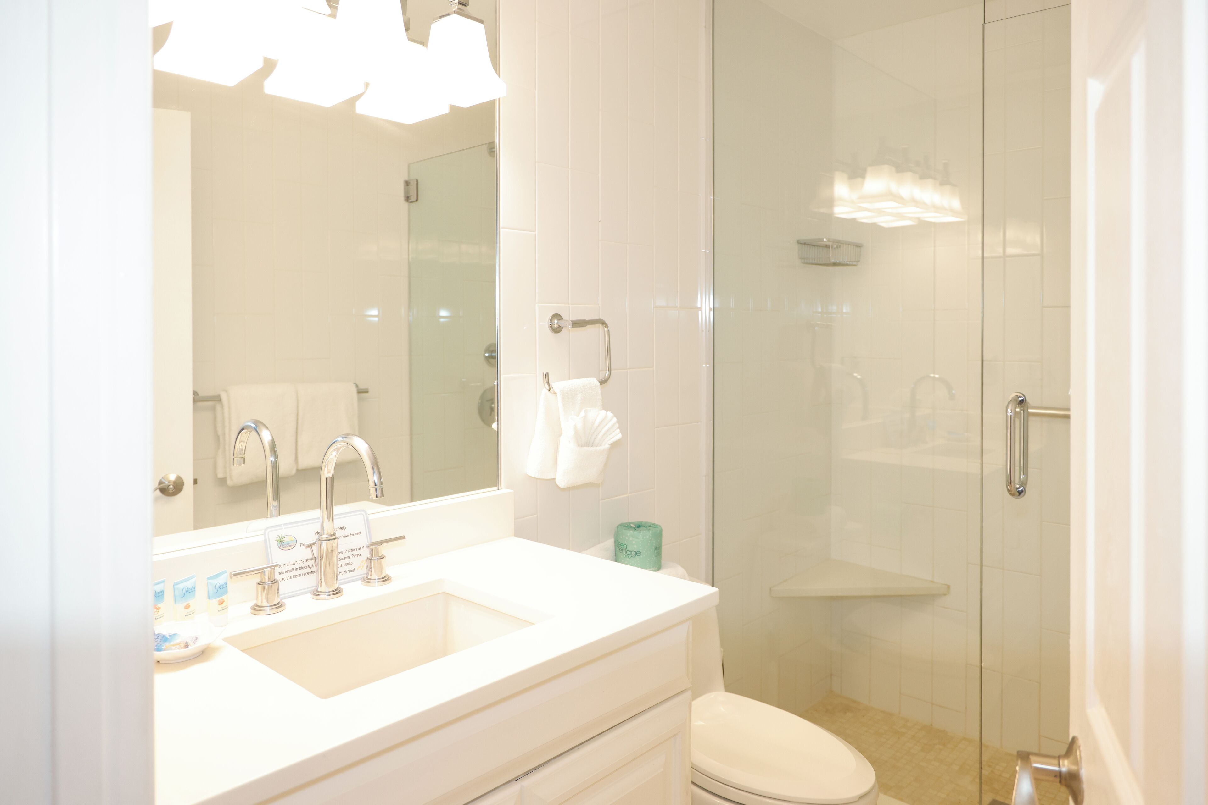 Un baño moderno con lavamanos blanco, espejo y cabina de ducha de vidrio.