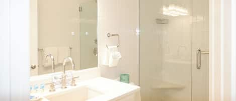 Un baño moderno con lavamanos blanco, espejo y cabina de ducha de vidrio.