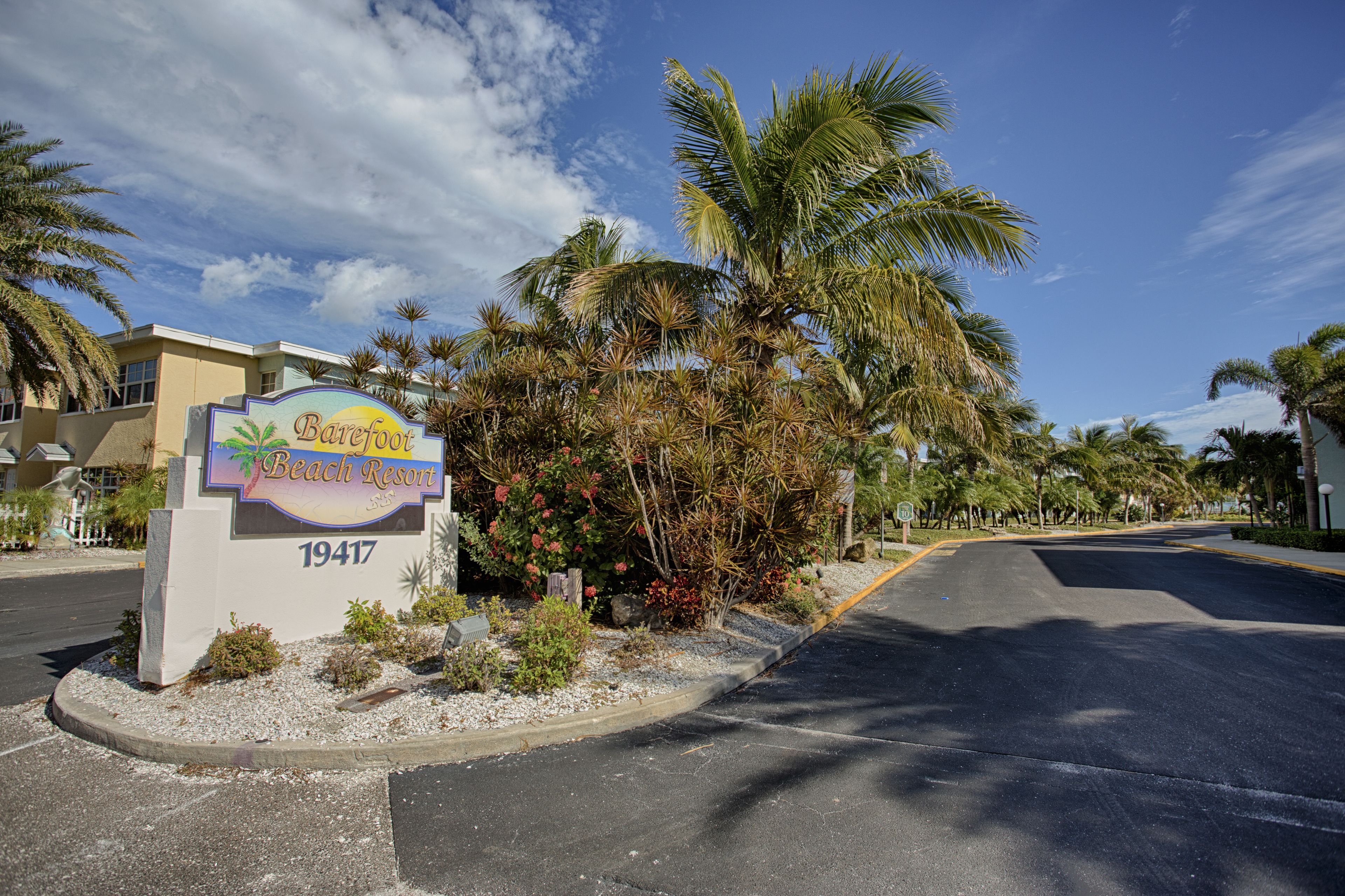 Un cartel para Barefoot Beach Resort con el número 19417, rodeado de palmeras y un cielo despejado.