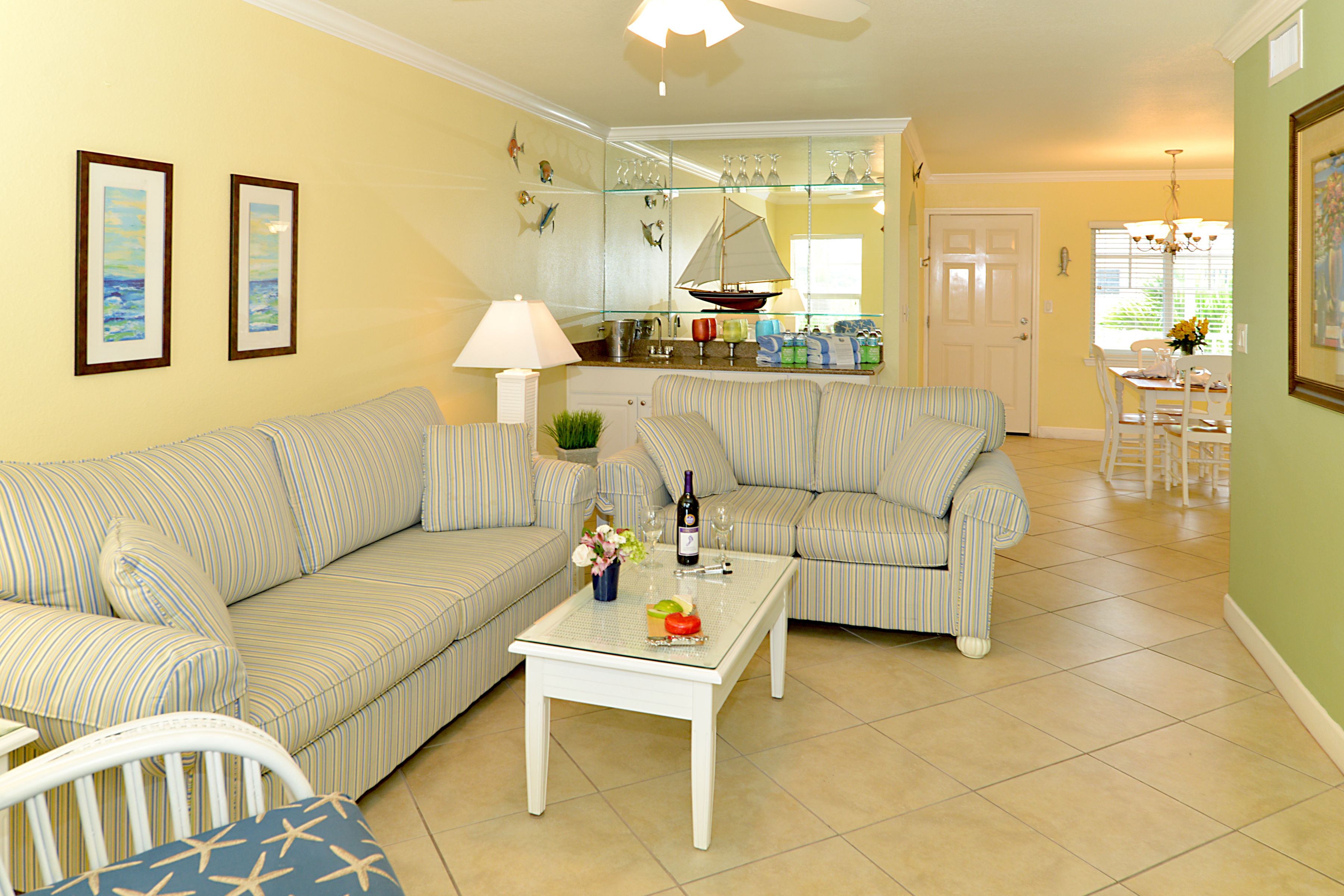 A living room with two striped sofas, a coffee table with a bottle and glasses, and a dining area with a table and chairs.