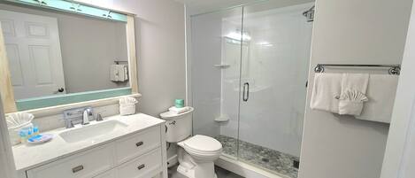 Een moderne badkamer met een douchecabine van glas, een witte wastafel met spiegel erboven en een toilet met handdoekhouder.