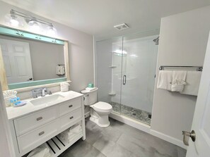 A modern bathroom with a glass-enclosed shower, a white sink with a mirror above, and a toilet with a towel rack.