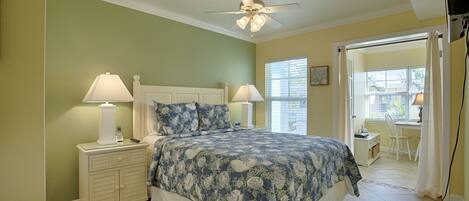 A bedroom with a bed, two bedside tables with lamps, a ceiling fan, and a window with curtains.
