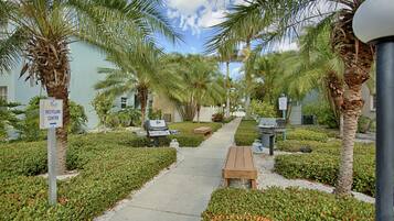 A pathway lined with palm trees and benches, leading to a building with a sign indicating a recycling center.