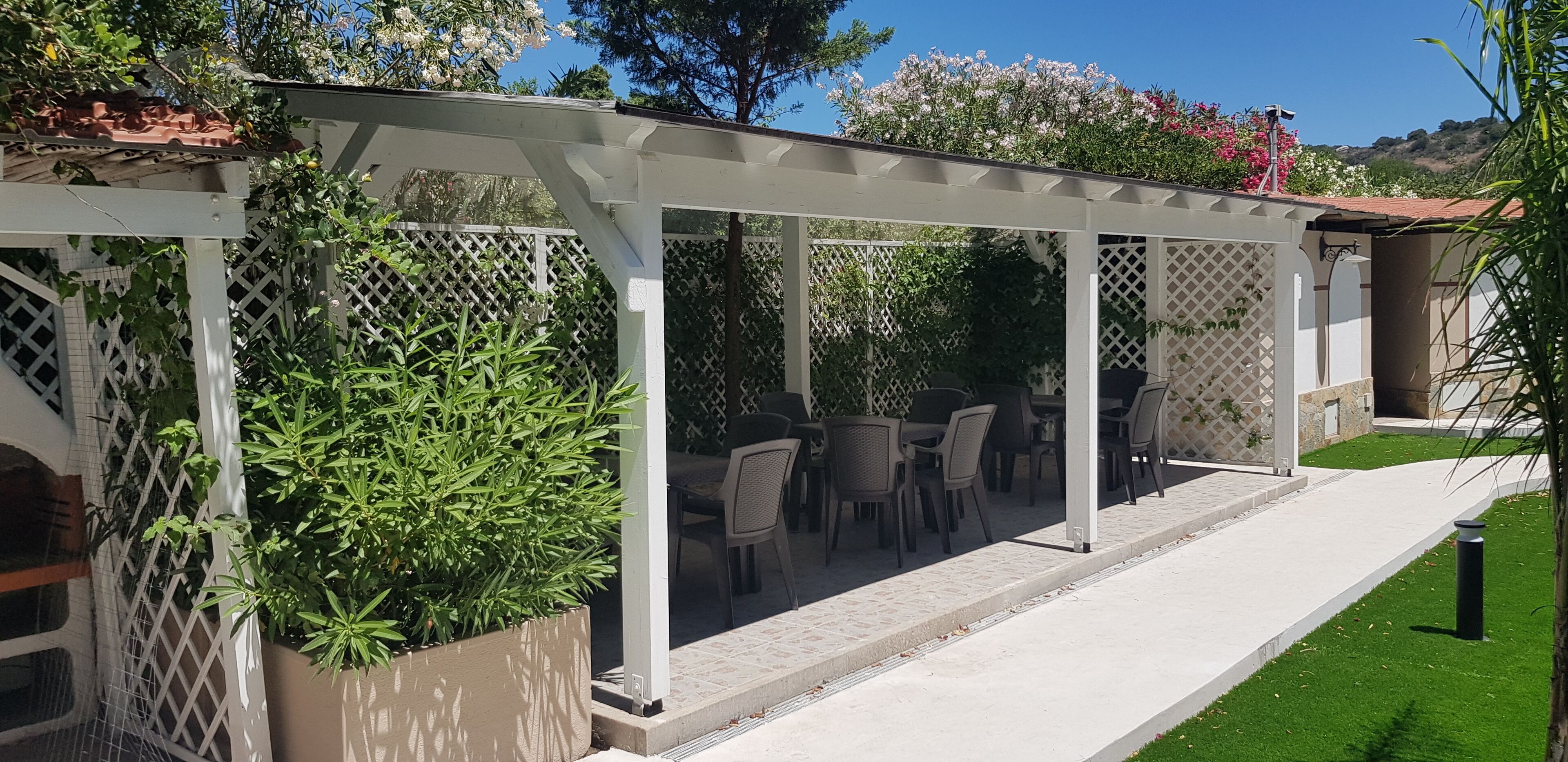 Ein überdachter Patio-Bereich mit einer Pergola, Sitzgelegenheiten im Freien und Topfpflanzen.