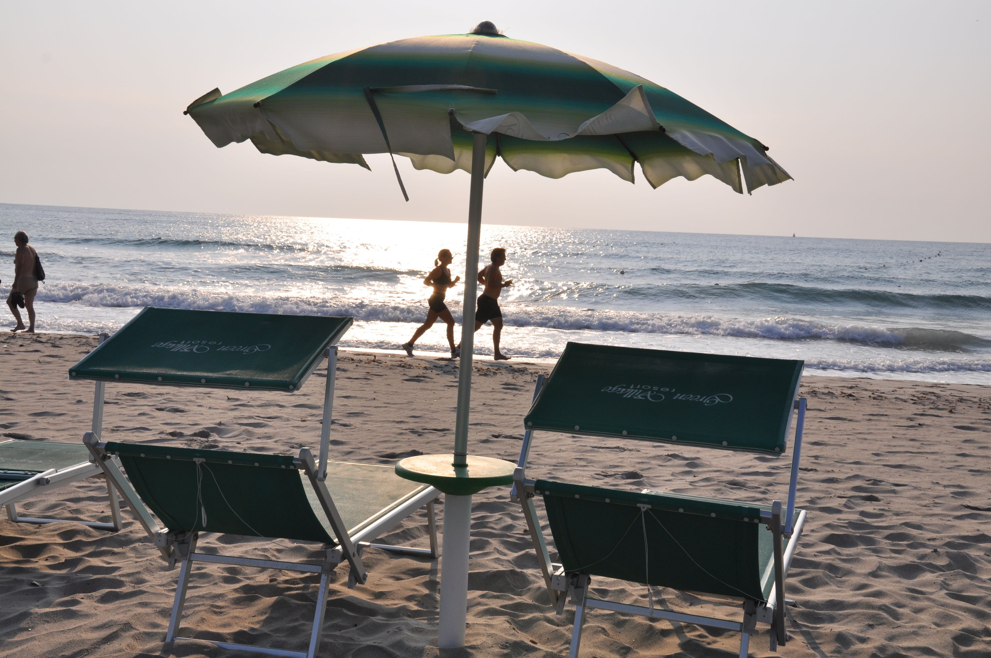 Beach chairs and an umbrella on a sandy beach with the ocean in the background.