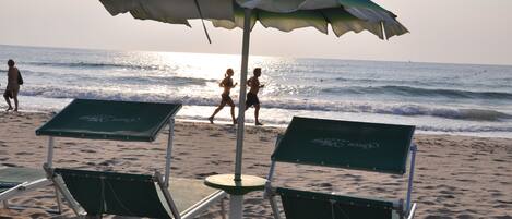 Beach chairs and an umbrella on a sandy beach with the ocean in the background.