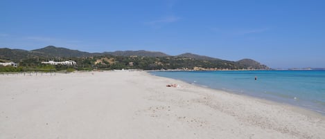 Una playa ancha de arena dorada, con agua azul cristalina y colinas a lo lejos.