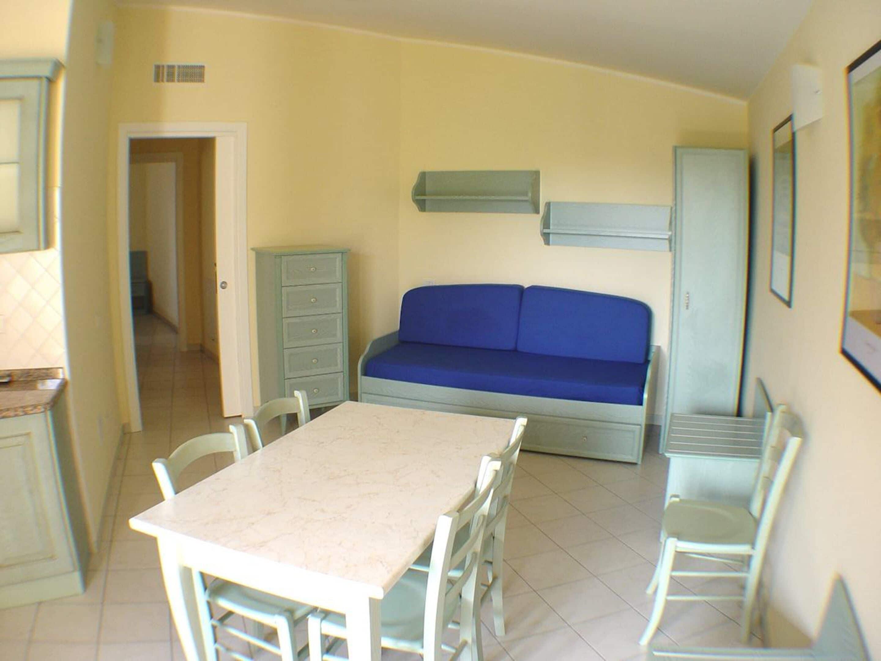 A compact living space with a dining table and chairs, a blue sofa, and a kitchenette area.