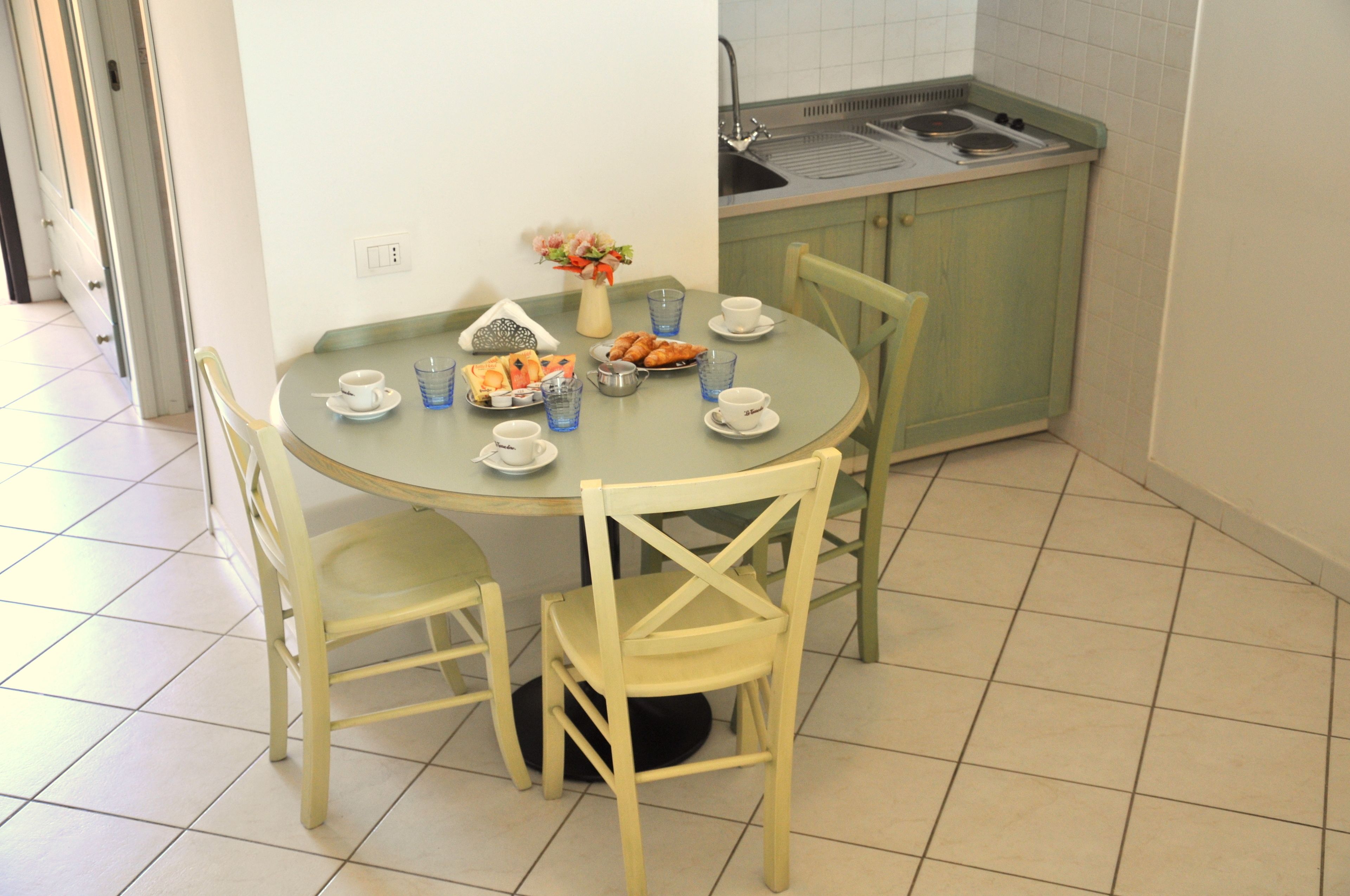 A dining area with a round table, two chairs, and a small kitchen area with a sink and stove.