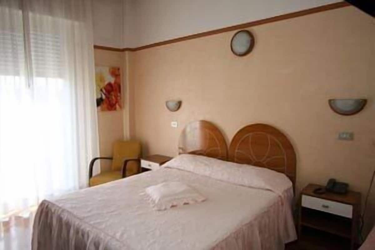 Una habitación de hotel con cama, una silla, una mesita de noche y un reloj de pared.