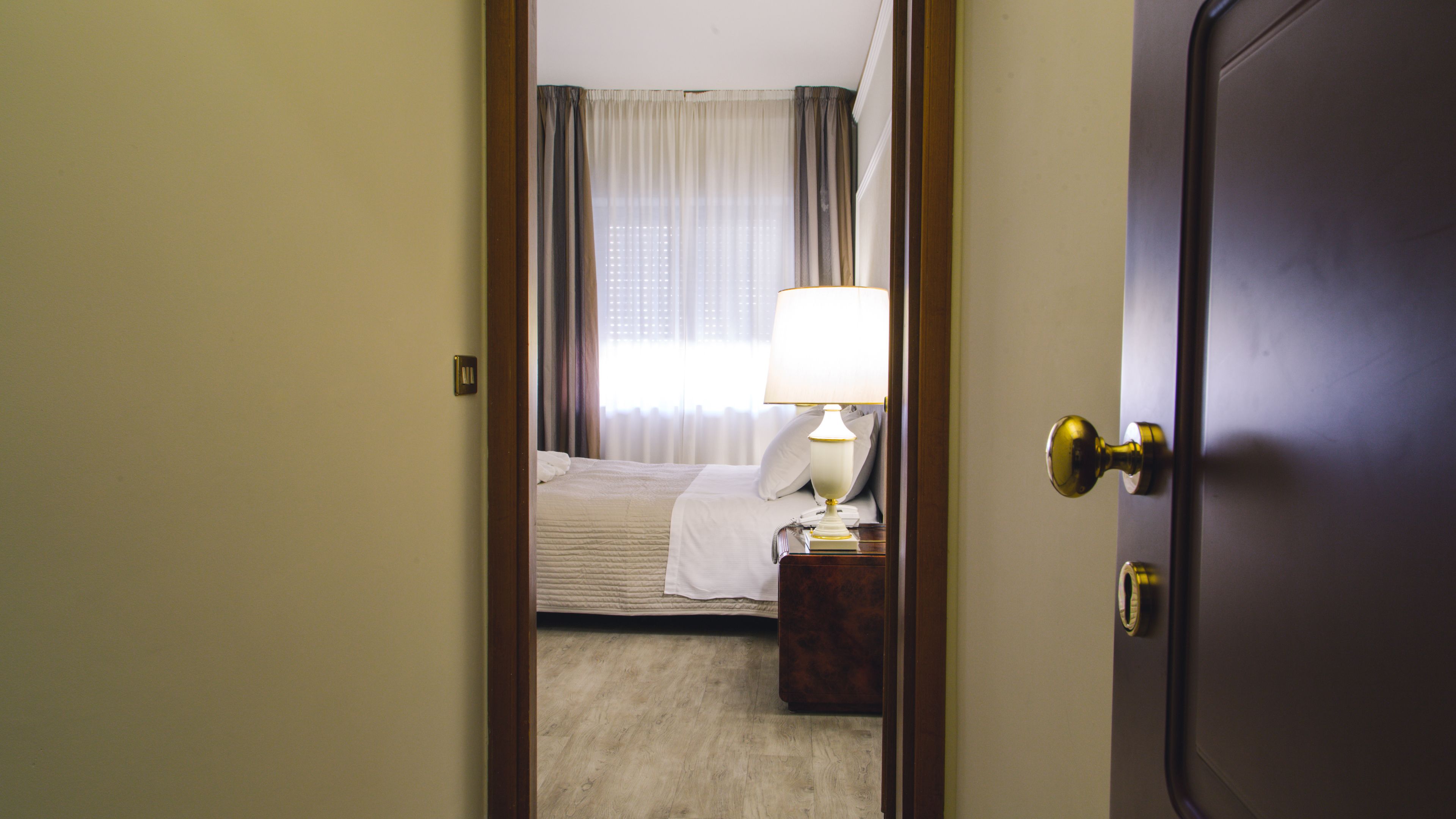 A hotel room with a bed, a bedside table with a lamp, and a door.