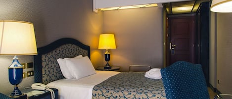 A hotel room with a bed, two bedside lamps, a telephone, a chair, and a door.