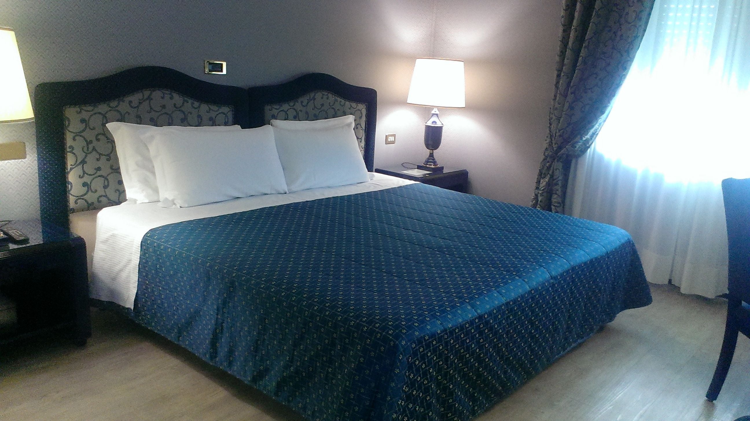 A hotel room with a large bed, a nightstand, a lamp, and a chair.