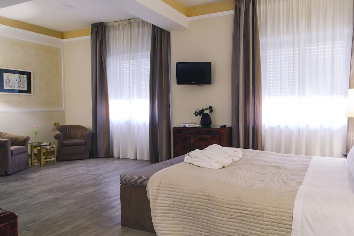 A hotel room with a large bed, a chair, a small table, a TV, and curtains.