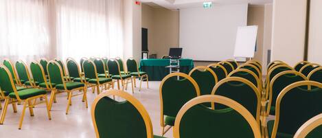 A conference room with rows of green chairs and a table with a laptop.