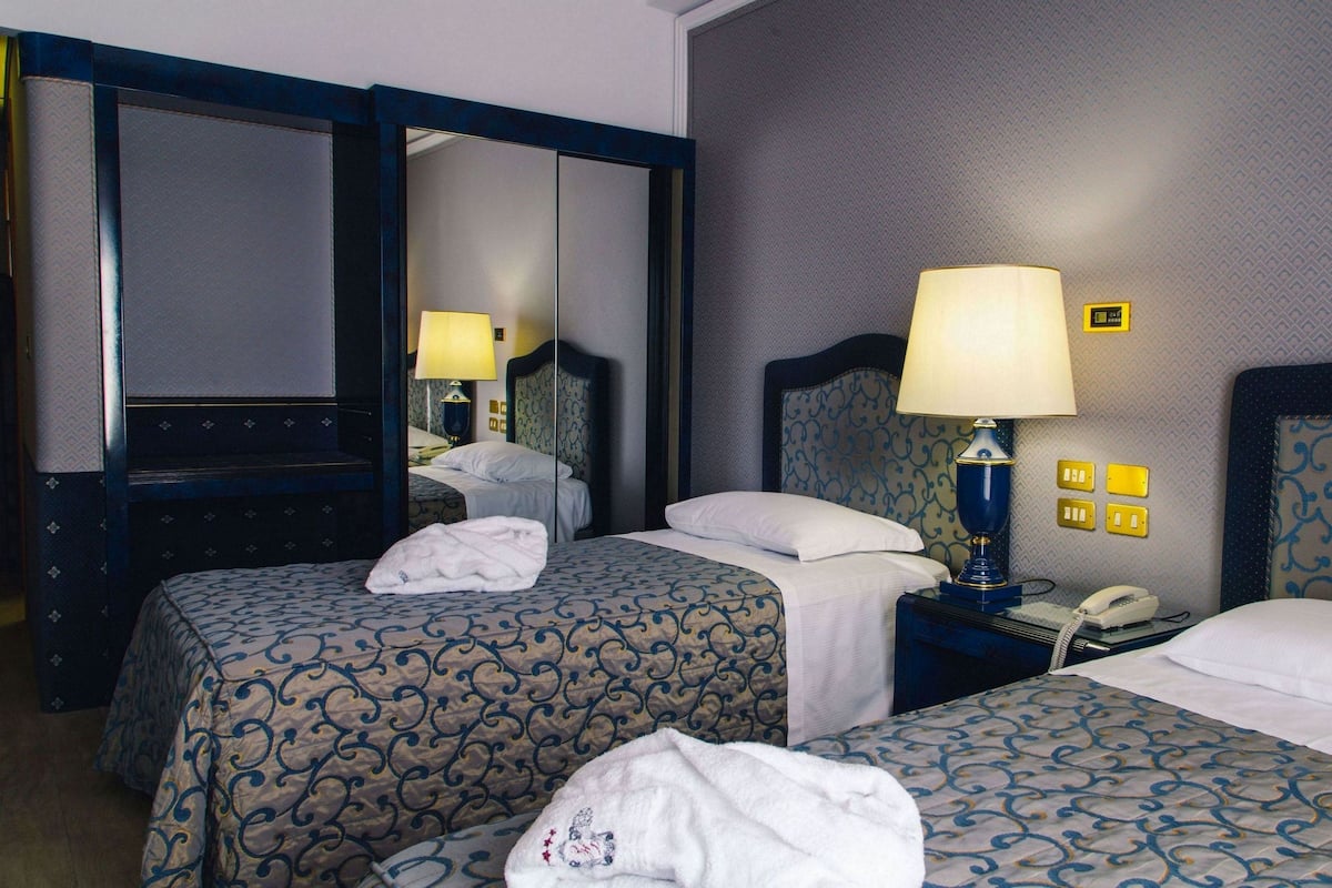 A hotel room with two beds, a mirror, a nightstand with a lamp, and a telephone.