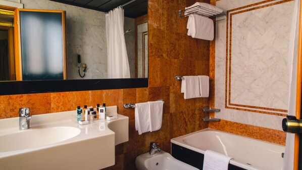 Une salle de bain avec deux lavabos, une baignoire et une douche. Des serviettes sont accrochées au mur et un miroir se trouve au-dessus du lavabo.