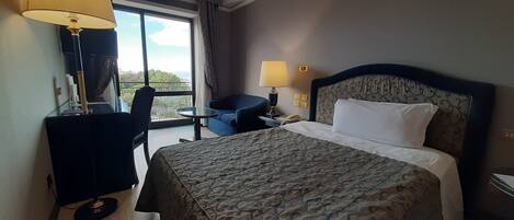 Habitación de hotel con una cama grande, un escritorio con lámpara, una silla y vistas al exterior.