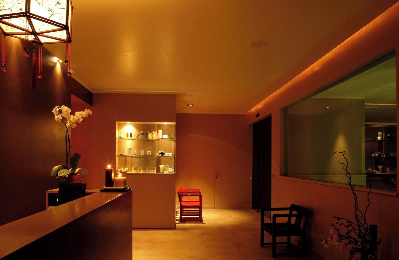 Un interno moderno con una reception, una teca in vetro, una poltrona rossa e un'ampia finestra.