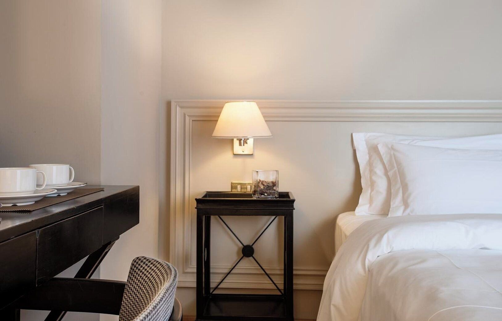A hotel room with a bed, a desk with a lamp, and a chair.
