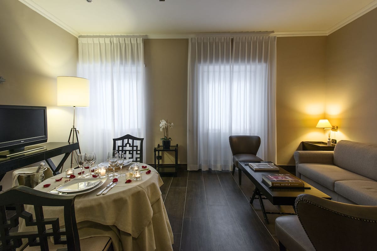 Una habitación de hotel con una mesa de comedor preparada para dos personas, un sofá, un televisor y una lámpara.