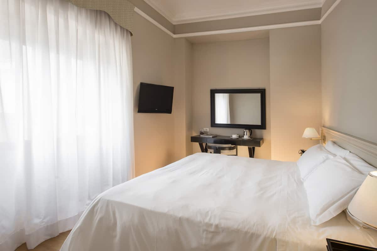 Habitación de hotel con cama, escritorio, televisor de pantalla plana, espejo y lámpara.